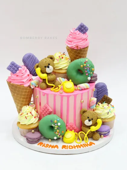 A "candyland" cake for twins, overloaded with edible treats like ice cream cones, donuts, macarons, and teddy bear figurines.