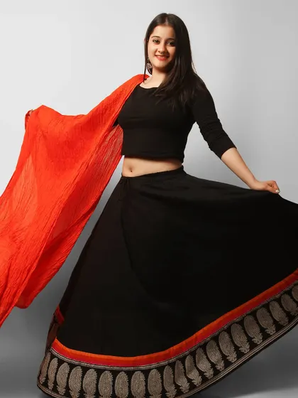 This fashion shot captures a model's joyful energy in a black and red ethnic lehenga. The movement in the skirt and dupatta creates a dynamic and visually engaging image perfect for a festive wear lookbook.