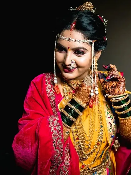 A portrait of the bride adjusting her jewelry, with a soft smile. The dark background makes her colorful attire and gold ornaments pop.