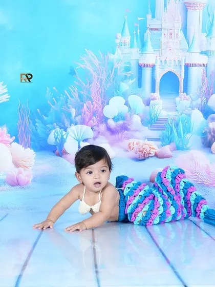 A beautiful shot of a baby in a mermaid costume, crawling on a set designed to look like the ocean floor. The underwater castle and coral create a perfect fantasy world.