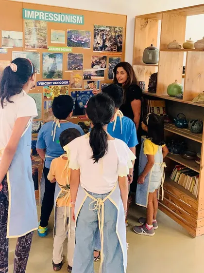 An instructor gathers students to discuss the Impressionist movement, using visual aids and examples to explain the concepts of light and color before they begin their Van Gogh inspired paintings.