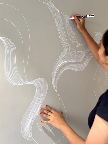 A work in progress shot of a minimalist line art mural. The flowing white lines on the grey wall create a sense of calm and movement.