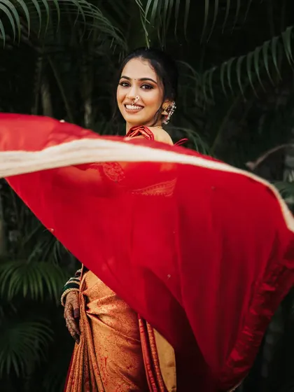 A dynamic shot of the bride, her red saree flowing in the wind as she smiles.