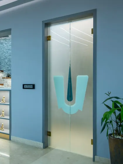 This puja room door features a custom frosted glass design with the 'Tirunamam' symbol, creating a modern yet reverent entrance to the sacred space.