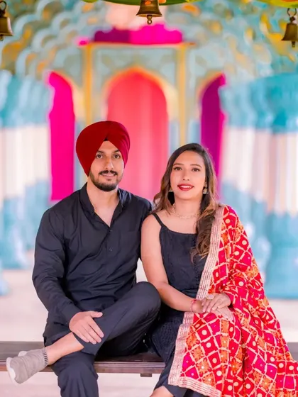 A happy portrait of a couple on a decorated swing. Their black outfits are beautifully contrasted by the colorful backdrop and the bride's vibrant dupatta.