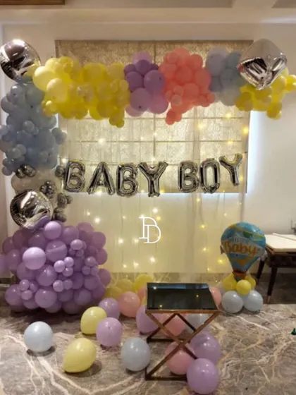 This "BABY BOY" home decoration uses a curtain of fairy lights as a backdrop for the foil balloons. The pastel balloon frame adds color and softness, creating a lovely photo spot.