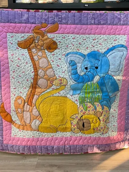 A whimsical baby quilt featuring large, friendly appliqué animals like a giraffe, lion, and elephant.