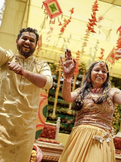 The couple dancing with joy at their Haldi ceremony, surrounded by festive decor.
