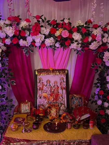 A beautiful floral arch with pink drapes created for a home pooja. The setup provides a perfect frame for the deity's picture.