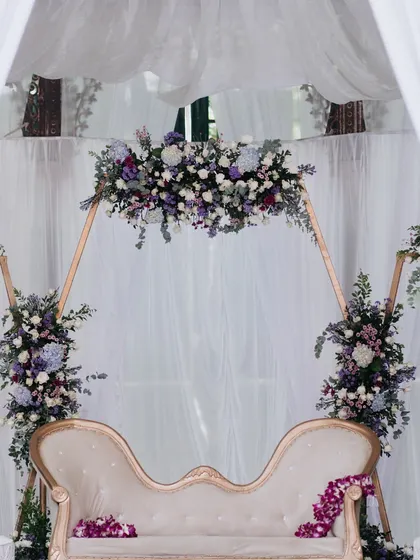 A simple and elegant reception stage with a floral arch in purple and white.