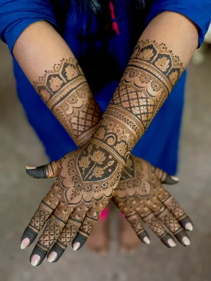 A crossed-hands pose of Supriya's engagement mehendi, emphasizing the beautiful forearm bands.