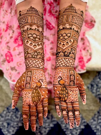 A grand bridal design featuring majestic peacocks on the palms and traditional motifs like elephants and temple domes on the forearms.