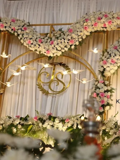 A detailed shot of an engagement stage backdrop, featuring a custom gold monogram, floral arches, and hanging bird decorations.
