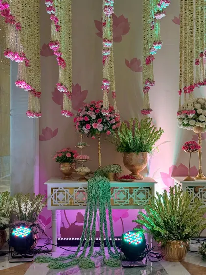 A wider view of a decor corner, where traditional elements are illuminated by soft, colorful lighting. The hanging floral strings and lotus-print wallpaper create a cohesive theme.