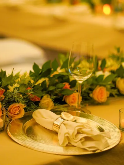 A close up of a single place setting, featuring a golden charger plate, a neatly folded napkin with a ring, and ambient candle lighting, showcasing my attention to detail.