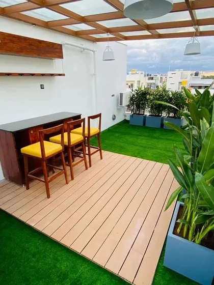 This is a complete terrace transformation, turning an unused urban rooftop into a stylish entertainment zone. The space features a custom bar, a wood-plastic composite (WPC) deck, ambient lighting, and lush planters, demonstrating how even compact areas can become luxurious extensions of the home.