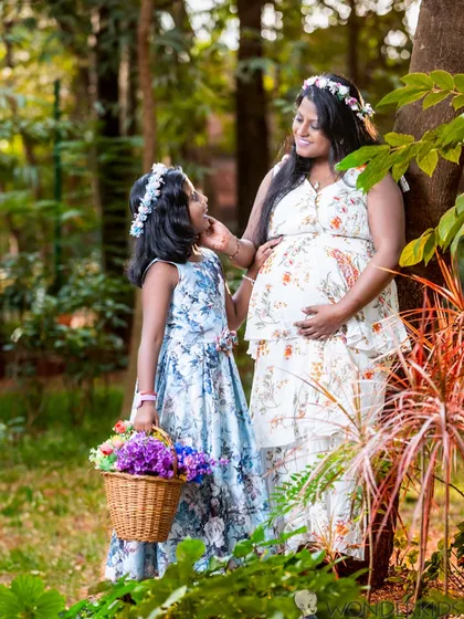 A lovely outdoor maternity photo of a mother and daughter wearing matching floral wreaths. The natural setting and their sweet interaction make this a cherished memory.