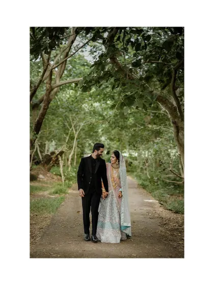 The couple walks hand-in-hand down a tree-lined path, creating a romantic and serene atmosphere.