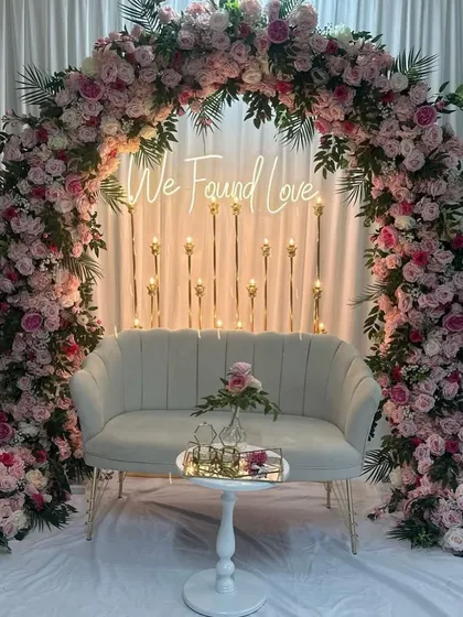 A full view of the romantic Roka ceremony stage, showing the floral arch, neon sign, and a comfortable loveseat for the couple.