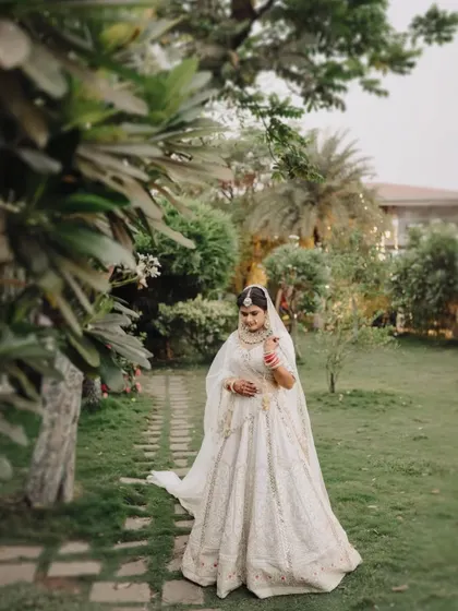 A beautiful portrait of the bride walking through a garden, her elegant white lehenga standing out against the lush greenery.