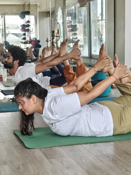 A line of TTC students practices Dhanurasana, showcasing the collective energy and focus of the group. The mirror reflection emphasizes the importance of self-observation and alignment.