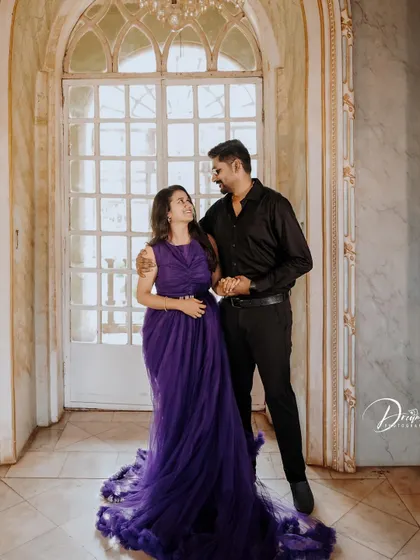 An elegant pre-wedding portrait in a grand hallway. The deep purple gown with its long, ruffled train adds a touch of royalty to the photo.