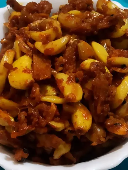 A bowl of my Ginger Garlic Pickle. The golden garlic cloves and pieces of ginger are coated in a thick, tangy masala, making it a flavorful and aromatic choice.