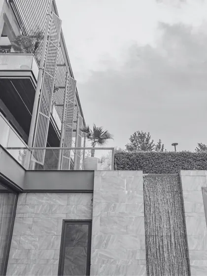 A black and white detail shot of a luxury residence, emphasizing the architectural lines and textures. The modern facade with its louvered screens and stone cladding showcases our focus on creating a harmonious blend of materials and forms.