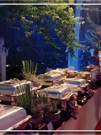 An evening buffet setup under moody blue lighting. We used elegant silver chafing dishes and dark floral arrangements to create a sophisticated and dramatic ambiance for this outdoor reception.