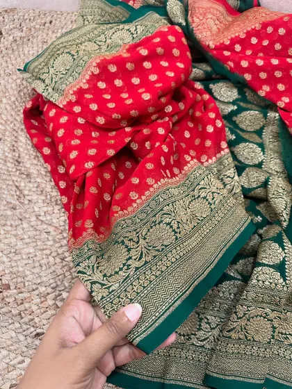 This red and green pure Banarasi Kadi georgette is a classic festive combination. The red body is adorned with gold butis, while the green pallu features heavy weaving.