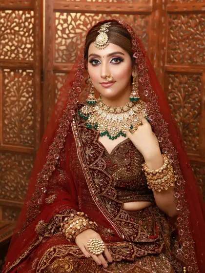 A full-coverage, glamorous bridal look in a deep maroon. The makeup is designed to be completely flawless for HD cameras, with defined eyes and a perfectly contoured face.