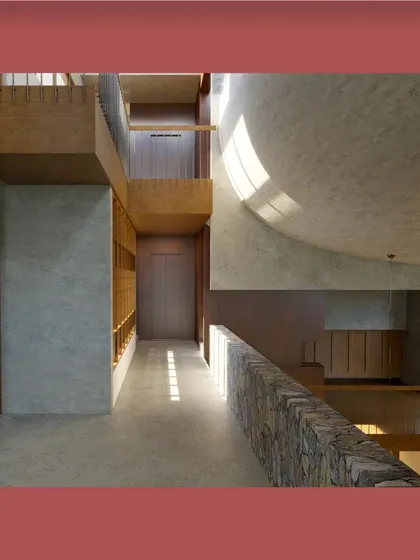 This visualization explores the interplay of light, shadow, and texture within the 'Belagavi Home'. A curved ceiling and a bridge-like corridor with a natural stone parapet create a dynamic and sculptural interior journey.