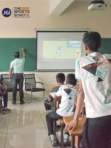 A teacher uses a cricket match video projected in the classroom to explain rules and tactics, blending sports analysis with academic learning.