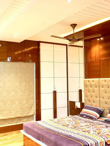 This bedroom features high-gloss wood veneer paneling and white wardrobe doors, creating a sleek and modern look. The tufted headboard adds a touch of softness and luxury.