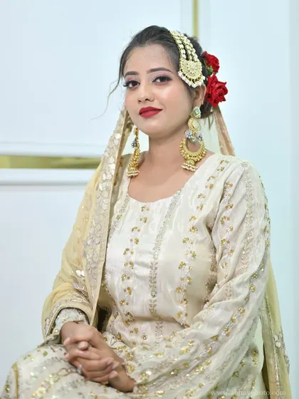 A seated portrait of a model in the ivory sharara set, her hair adorned with red roses and a traditional passa.