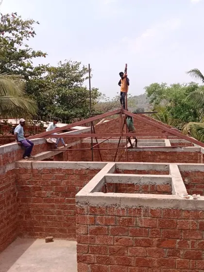 Workers raising the steel roof structure for Organic Square. This image captures the blend of modern construction techniques with local, load-bearing stone walls.
