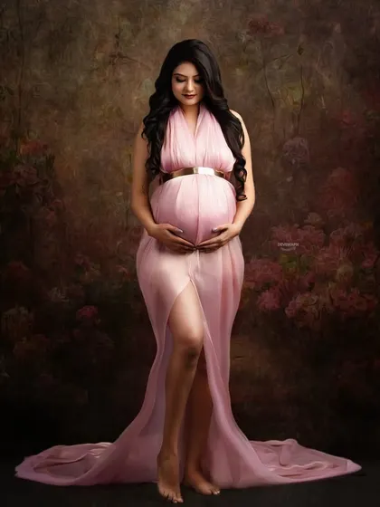 A classic fine art portrait against a painterly brown backdrop. The sheer pink gown, gold belt, and gentle pose evoke a sense of timeless grace and beauty.
