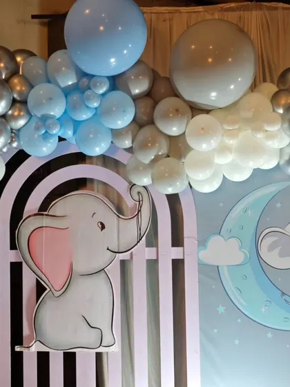 A cute elephant cutout peeking over an arched panel, part of a larger baby elephant themed setup.