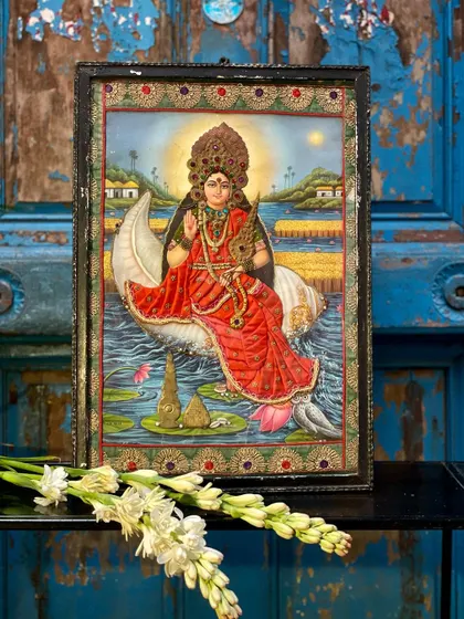 A cloth oleograph of a goddess on a conch shell, framed and displayed with flowers. This is one of my exclusive home decor pieces, where vintage prints are adorned with extensive embroidery.