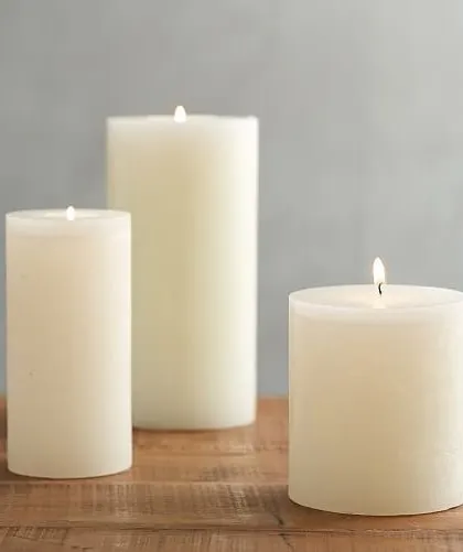 A collection of lit ivory pillar candles on a wooden surface, demonstrating their warm and gentle light. These are perfect for creating a serene and calming environment in spas or for candlelight dinners.