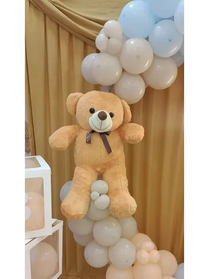 A soft teddy bear prop nestled into the balloon garland on the welcome ring.