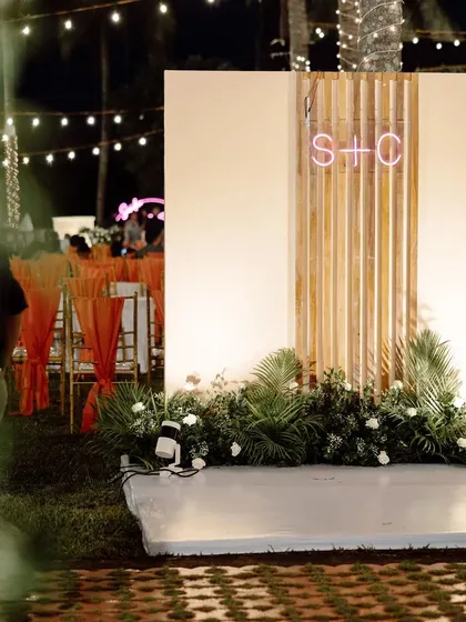 A modern and minimalist photo booth idea. A simple wall with lush greenery is personalized with the couple's initials in a glowing neon sign.