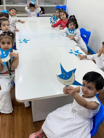 Our Blue Butterfly class celebrating Eid. The children, dressed in white, hold up their moon and star crafts, learning about the festival's symbols and spirit of togetherness.