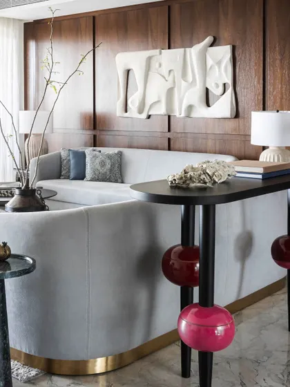 A unique side table with fuchsia pink spheres adds a pop of playful color, creating a striking yet complementary contrast to the cool tones of the living room and the abstract 3D wall art.