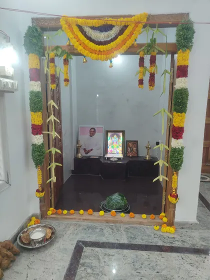 A traditional floral decoration for the main door of a home during a housewarming ceremony. The frame is adorned with garlands of marigold, mango leaves, and other flowers.
