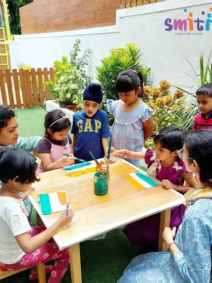 A teacher oversees a group of children painting their flags, fostering a collaborative and festive atmosphere for Independence Day.