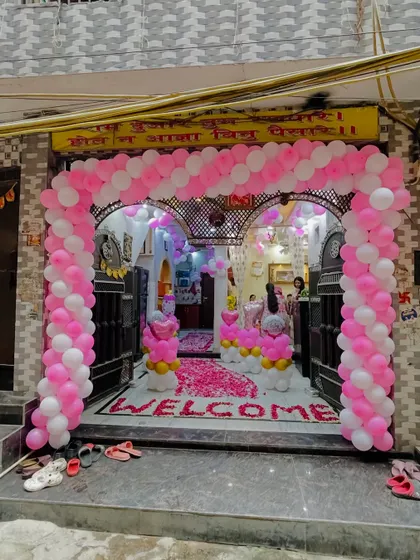 A grand 'Welcome Baby' entrance decoration in pink and white. The balloon arch frames the doorway, and the floor is covered with a rose petal 'WELCOME' message.