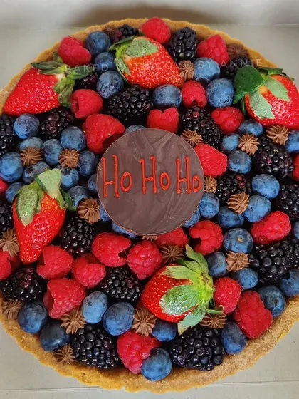 My Signature Dark Chocolate Tart decorated for the holidays. It's topped with fresh winter berries and a festive "Ho Ho Ho" chocolate plaque, making it a perfect Christmas centerpiece.