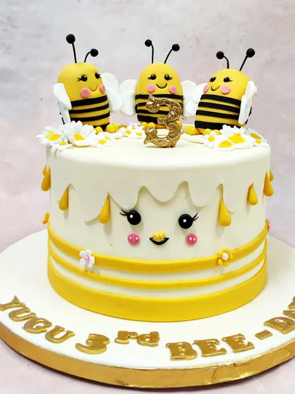 We create a buzz with this sweet-as-honey bumblebee theme cake. Three smiling bees sit atop a cake with dripping honey details and a cute face, making for an un-bee-lievably adorable "Bee-Day" celebration.