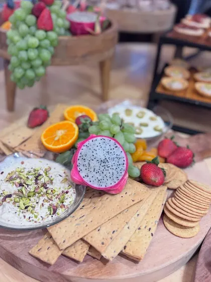 A vibrant charcuterie board featuring a colorful mix of fresh fruits like dragon fruit and strawberries, paired with multi-grain crackers and a creamy pistachio-topped dip. A feast for the eyes and the palate.